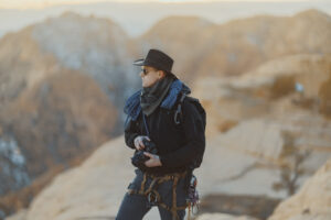 Climbing photographer in Utah backcountry wearing rope and harness while holding camera at Yant Flat during golden hour
