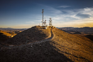 Communication towers and equipment buildings on elevated rocky terrain captured through professional commercial photography for telecommunications industry marketing