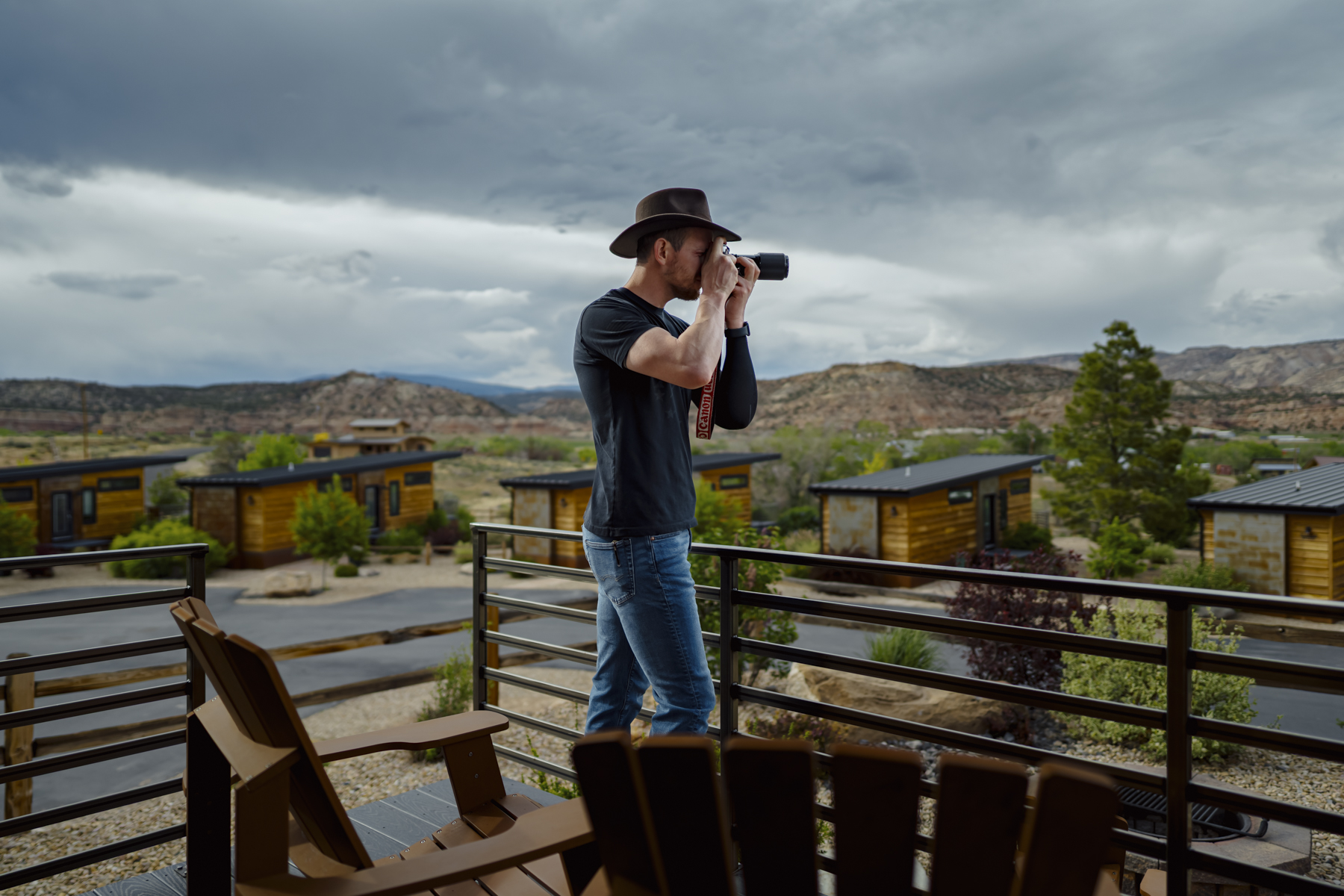 Photographer in hat standing on deck with camera in Escalante Utah surrounded by desert cabins and stormy skies