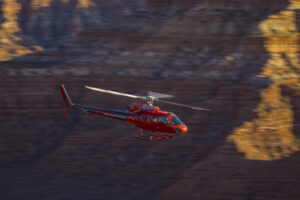 Red helicopter flying over Utah desert terrain with golden canyon walls captured through professional commercial photography for tourism marketing