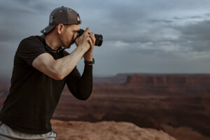 Utah landscape photographer capturing sunset scene in Moab while standing at canyon rim with Sony camera in hand