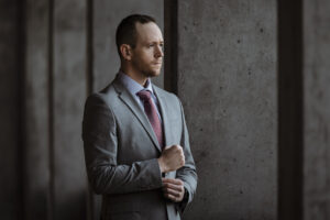 Professional Utah brand photographer in gray suit standing against concrete wall showcasing confident leadership and business identity