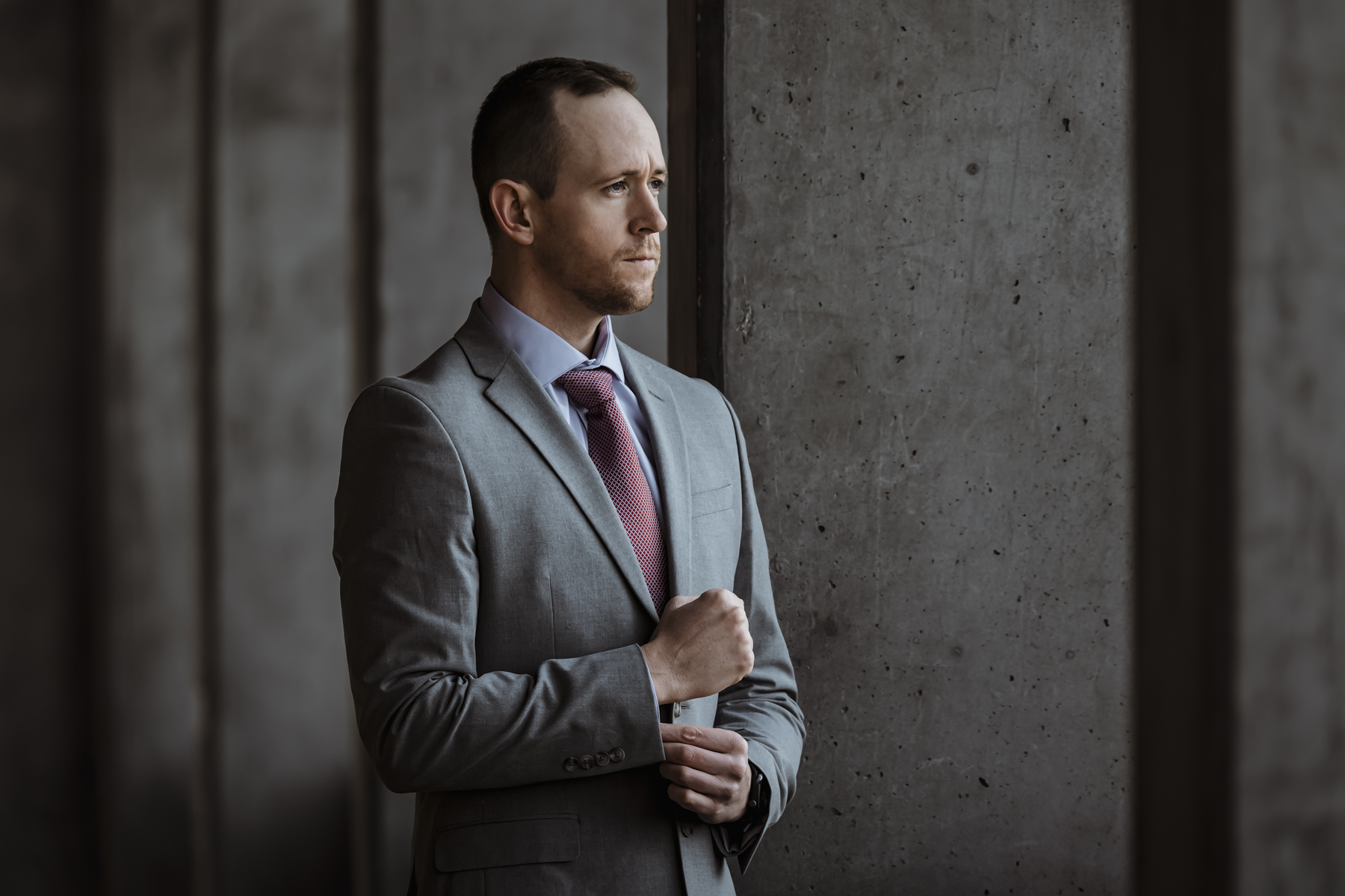Professional Utah brand photographer in gray suit standing against concrete wall showcasing confident leadership and business identity