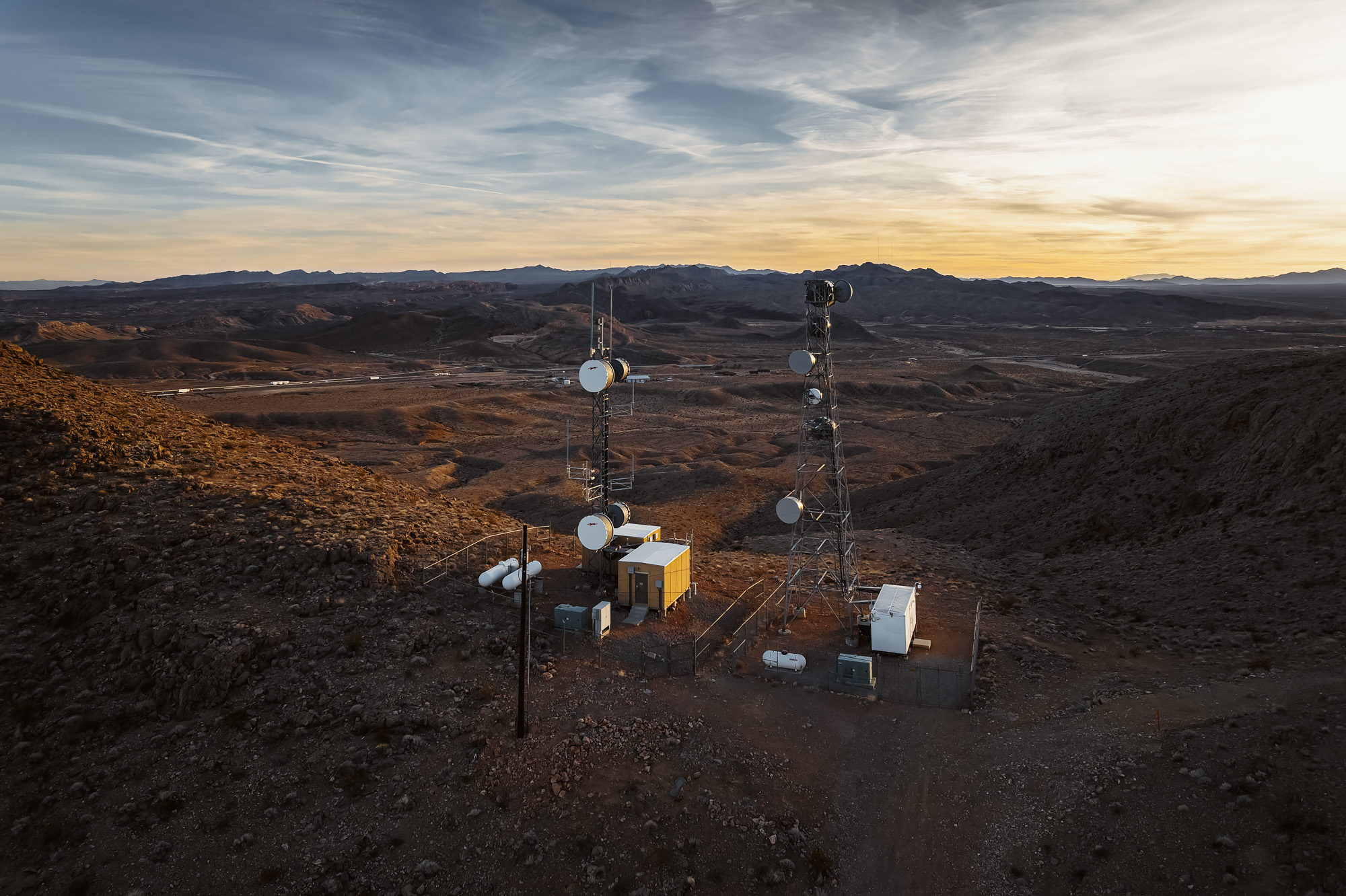 Cell tower facility with multiple communication towers and equipment buildings on elevated desert terrain captured by professional commercial photographer