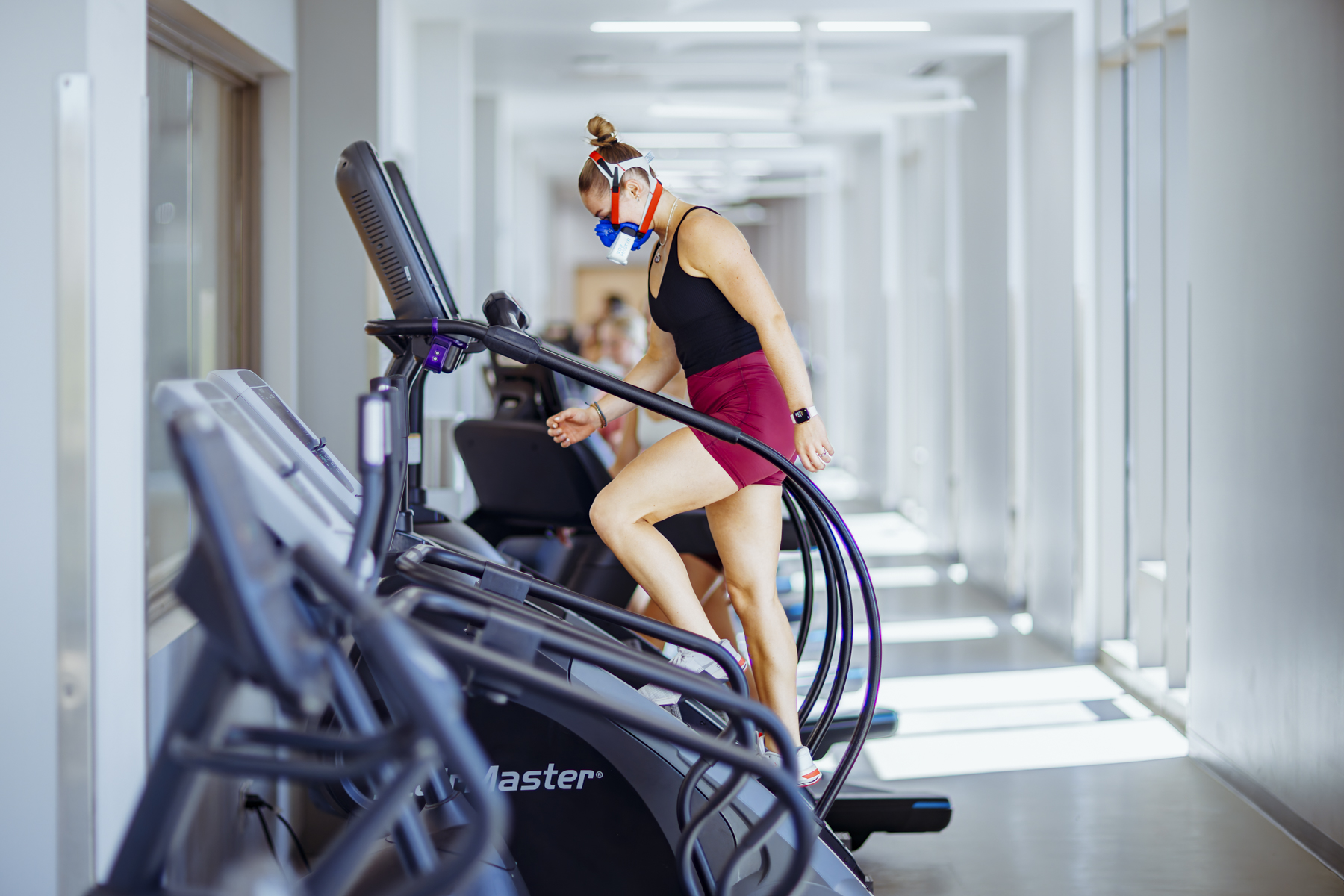 Female athlete using stair stepper while wearing VO2 Master metabolic analyzer during cardio performance test in modern clinical fitness center