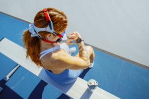 Overhead view of female athlete wearing VO2 Master mask checking smartwatch during rest after workout session on outdoor bench with water bottle