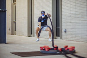 Male athlete performs high-intensity battle rope workout while wearing VO2 Master metabolic analyzer for fitness performance testing in clinical gym setting