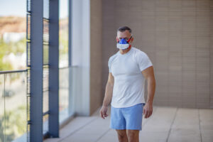 Male athlete standing in gym facility wearing VO2 Master metabolic analyzer for active performance testing with natural light and modern health setting