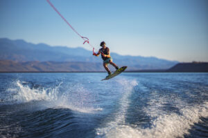 Professional wakeboard jump commercial photography showing aerial action above Utah lake water with desert mountain scenery for adventure tourism marketing