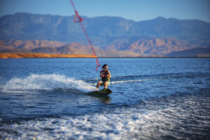 Water sports commercial photography of wakeboarding action on blue lake water with Utah desert mountain landscape captured for adventure center marketing