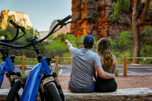 Couple relaxes with Zion Peddler e-bikes while admiring red rock cliffs in Zion National Park during a scenic electric bike adventure