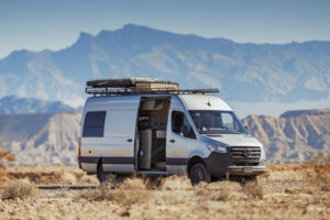 Custom-built Mercedes camper van parked in Southern Utah desert with open door revealing interior living space and mountain backdrop