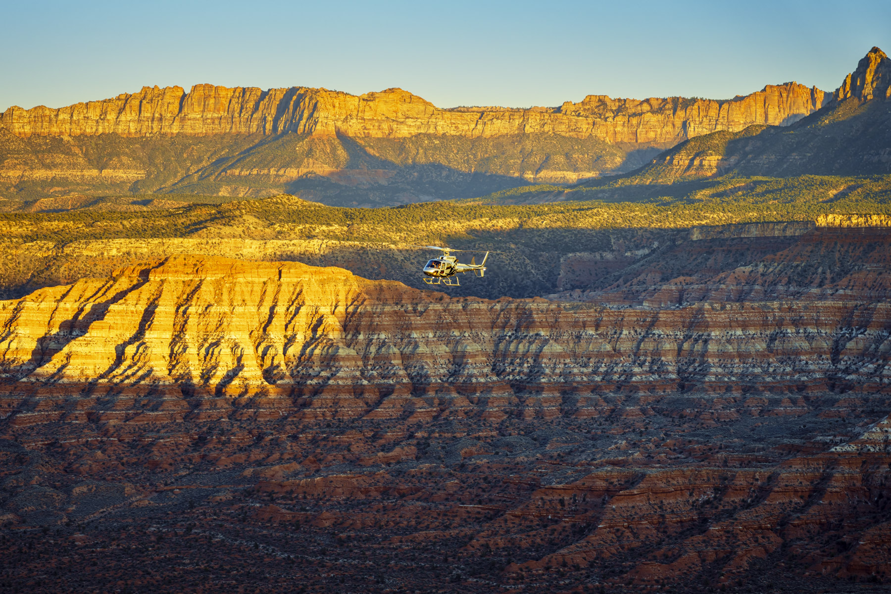 A helicopter flies over layered desert cliffs in Zion during golden hour, captured for aviation tourism branding and marketing