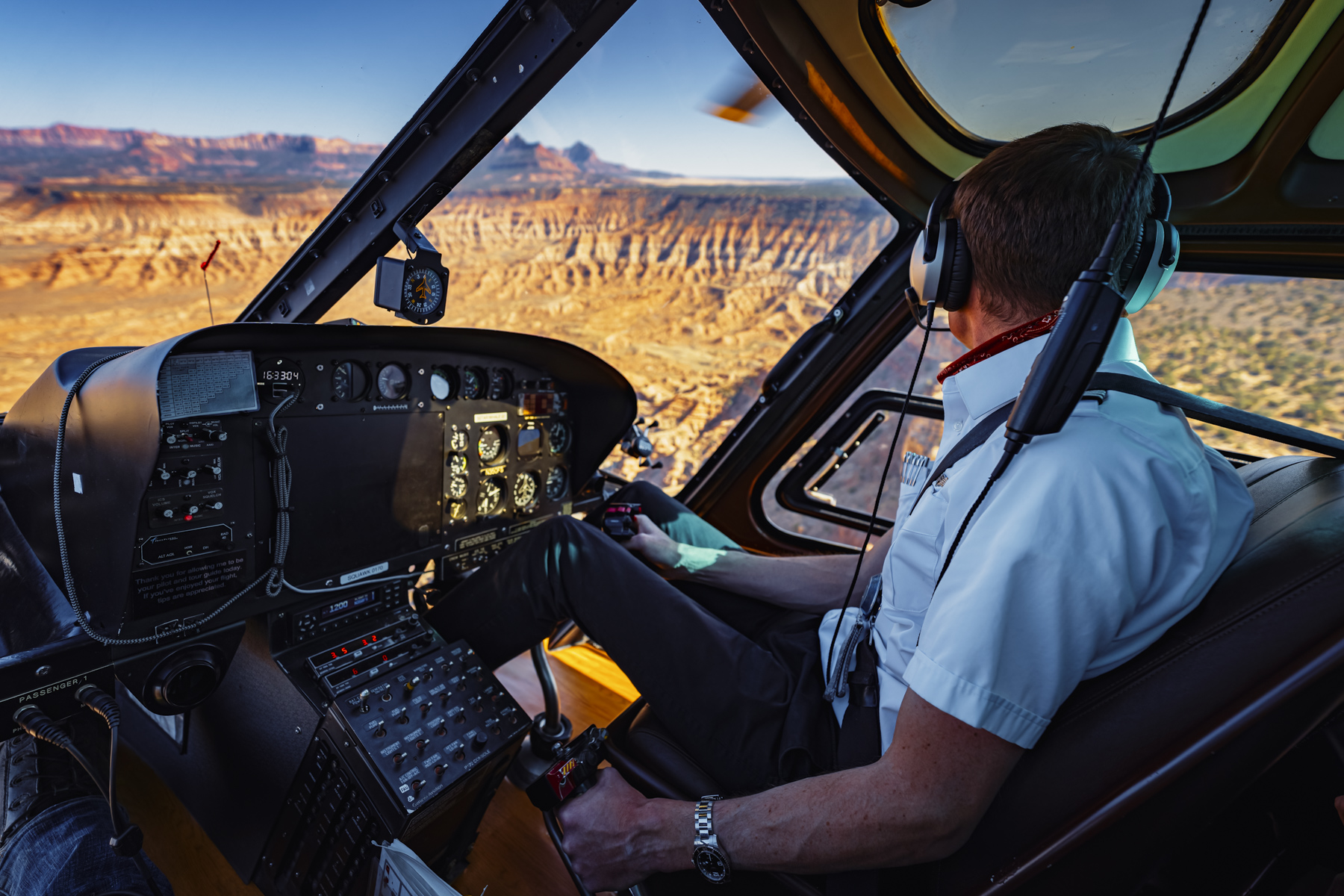 Helicopter pilot in cockpit with instrument panel and Utah red rock landscape visible through windows during commercial aviation photography