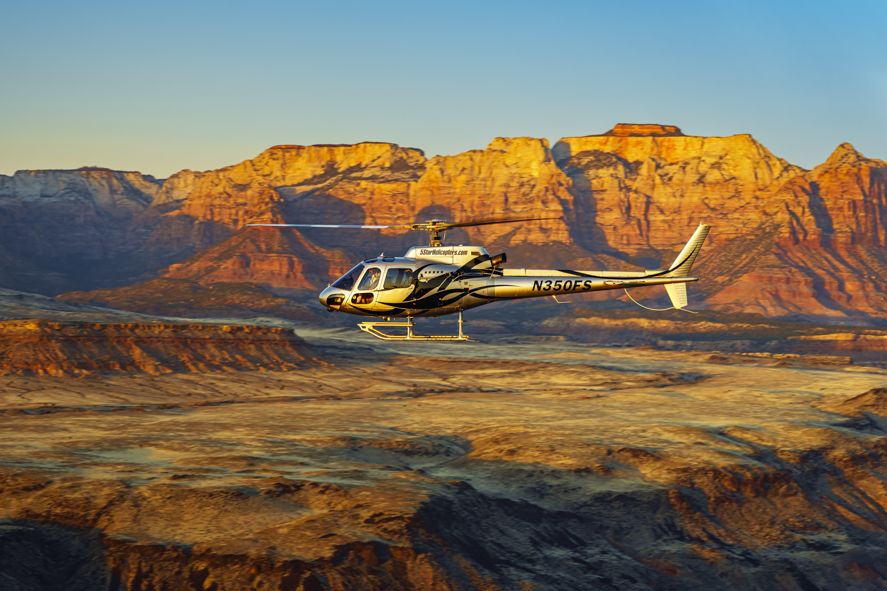 Commercial helicopter flying past golden illuminated Zion cliffs showcasing aviation tourism marketing and professional commercial photography services