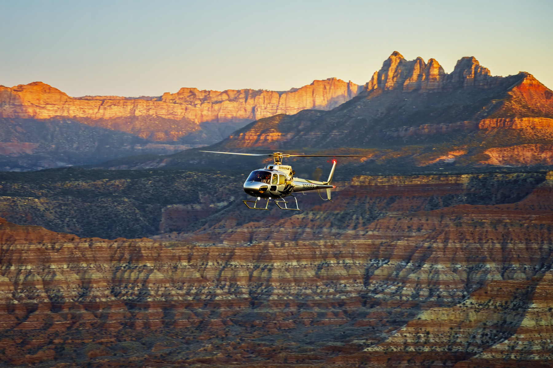 Commercial helicopter flying through Zion valley during sunset showcasing aviation tourism marketing and professional commercial photography services