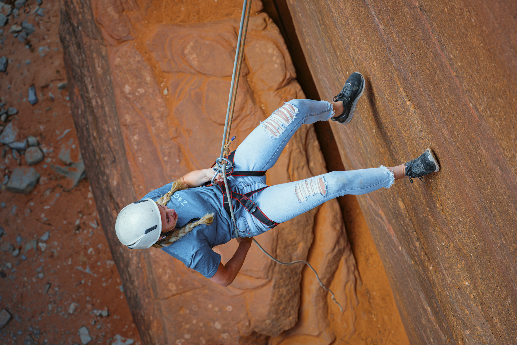 Woman rappels down a sunlit red rock wall on rope, a strong fit for outdoor brand photography and commercial lifestyle photography.