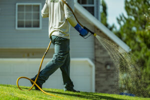A lawn care worker sprays treatment across a green lawn in front of a residential home.